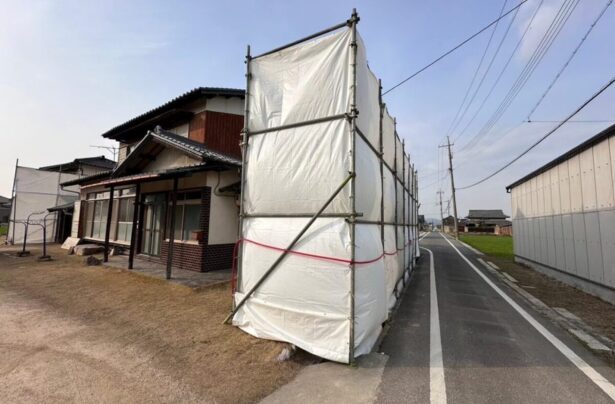 解体工事中の近隣トラブルを防ぐため養生シートを設置した住宅現場の様子