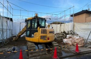 解体工事で近隣トラブルを防ぐため養生シートを設置し重機作業を行う住宅現場