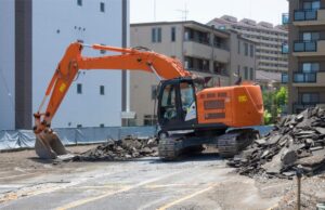 重機でコンクリートやアスファルトの駐車場を撤去している解体工事の様子